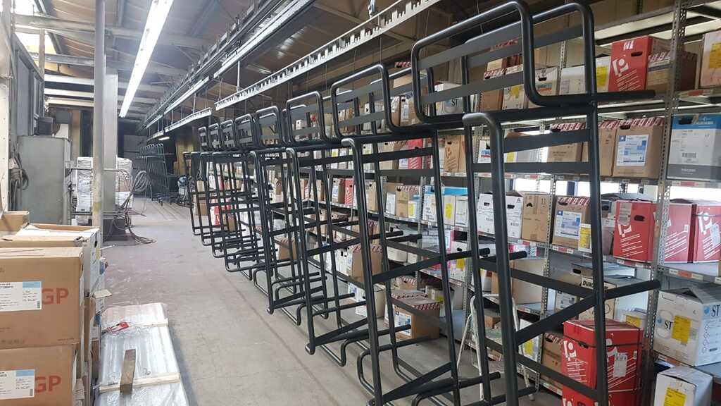 Mehrere schwarze Rollwagen stehen vor Regalen mit bunten Kartons in einer Lagerhalle