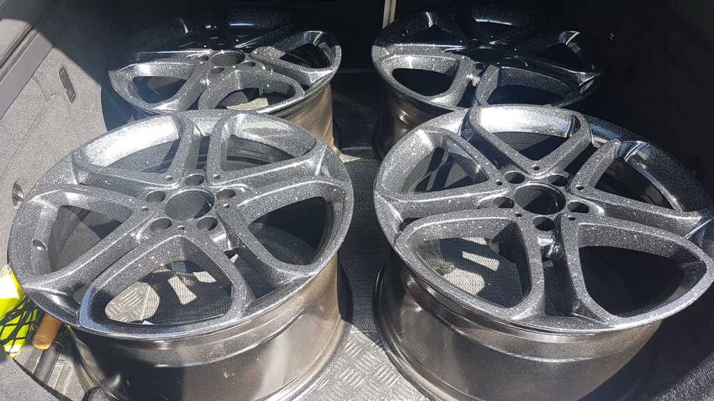 Vier glänzende schwarze Felgen mit funkelndem Finish liegen nebeneinander im Kofferraum